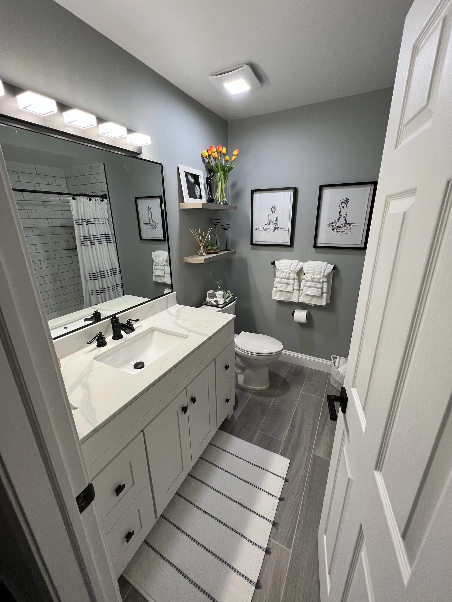 Hall bath with white shaker vanity, black hardware, framed art trio, and subway tile shower