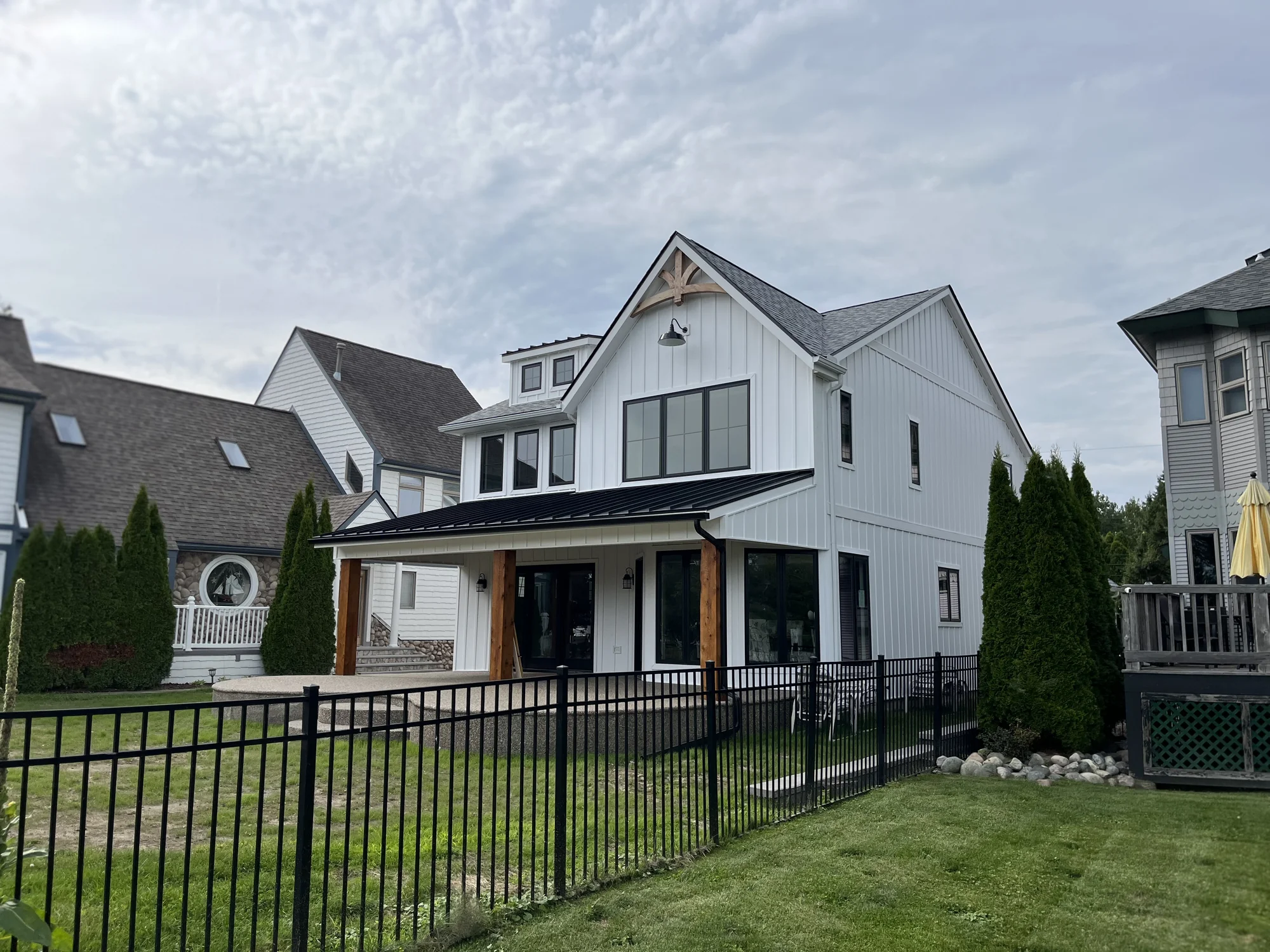 Same home after exterior remodel — board-and-batten siding, dormer with arched bracket, expanded covered porch with metal roof, and wood column accents