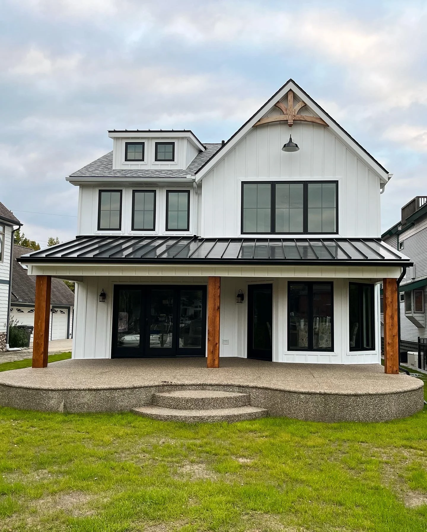 Same home after exterior remodel — board-and-batten siding, dormer, arched bracket, metal porch roof, and wood column accents
