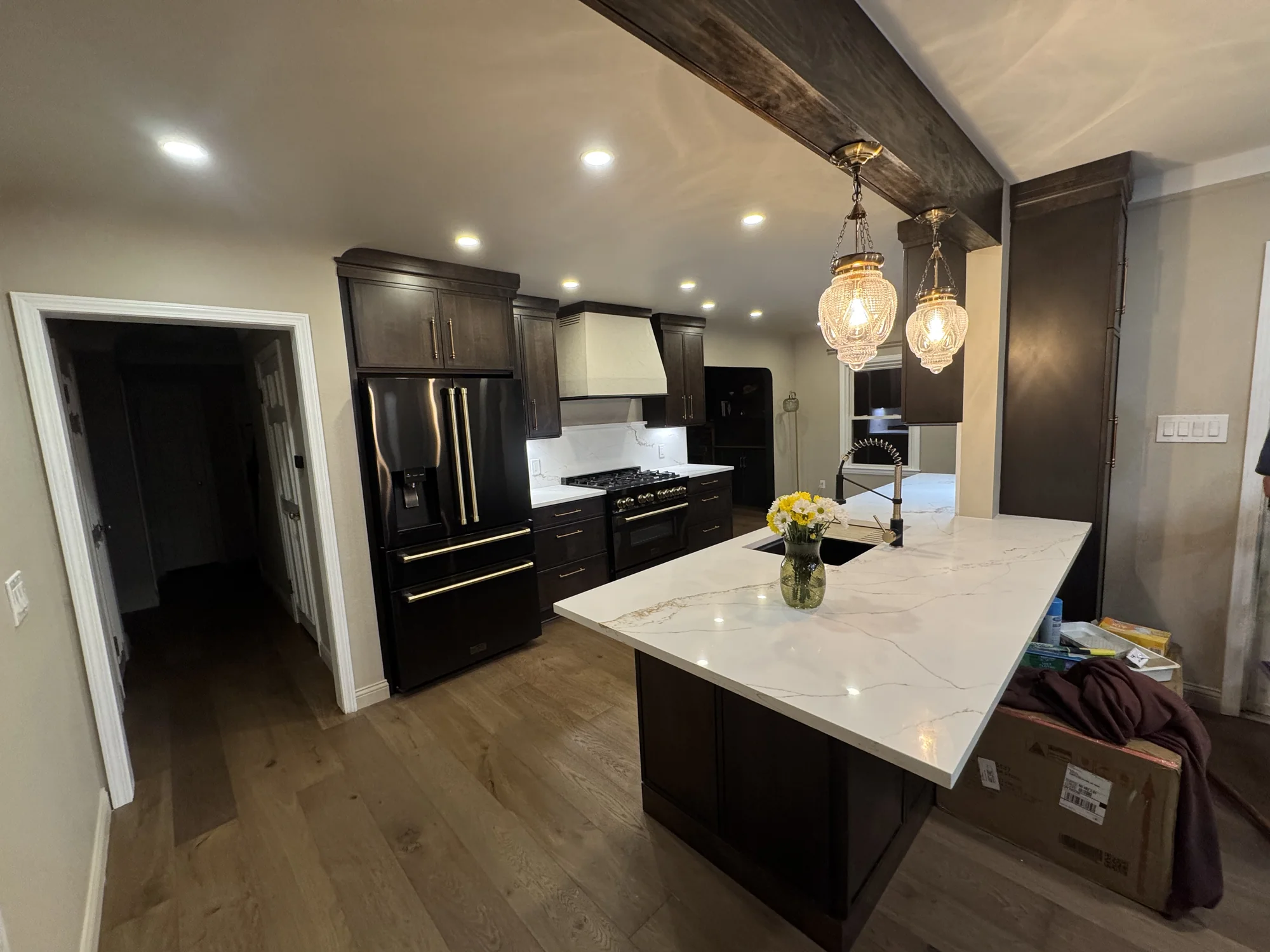 Kitchen island with white quartz waterfall counter, black appliances, dark cabinets, and gold chandelier pendants