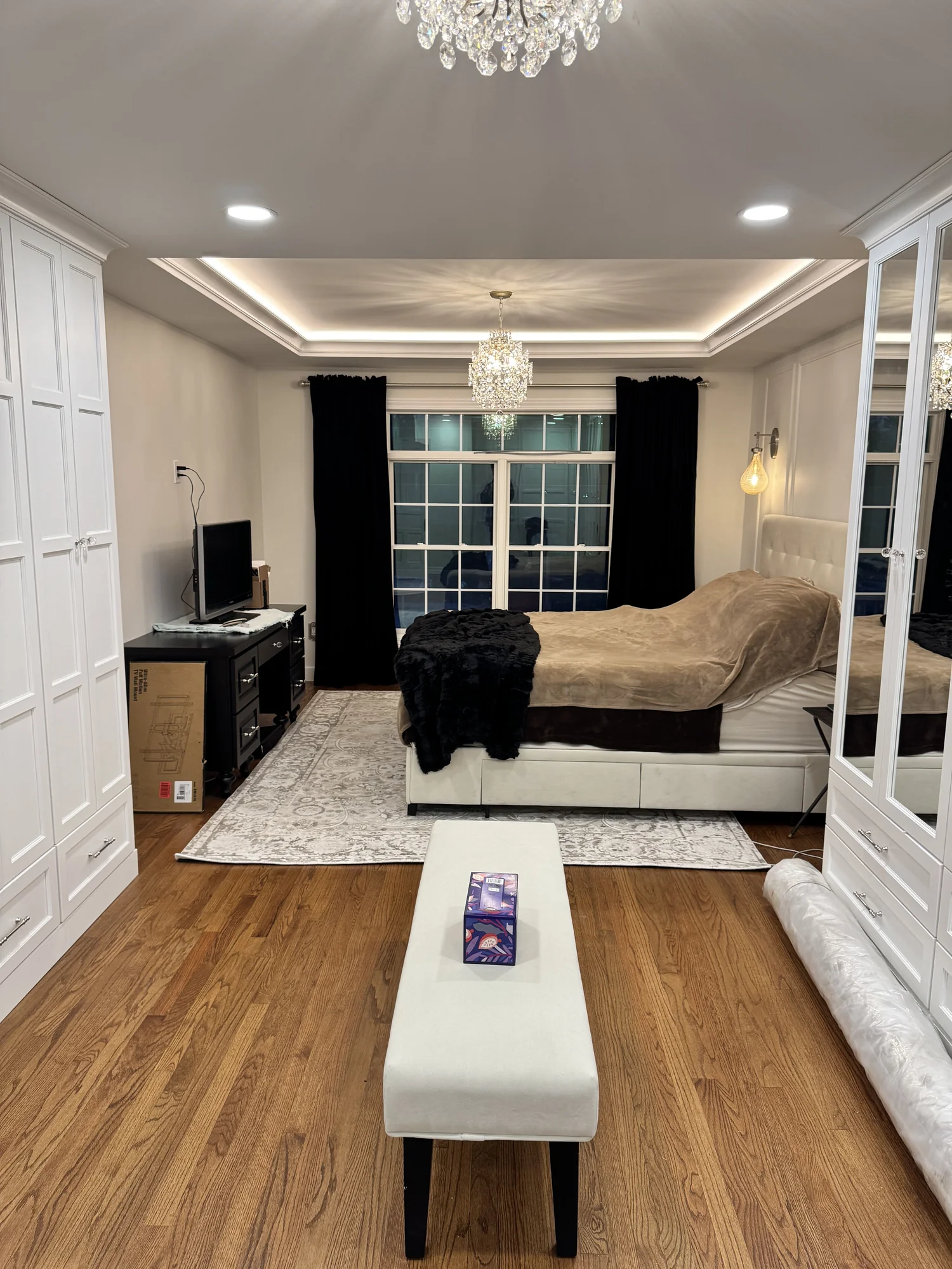 Primary bedroom addition with white built-in wardrobes, tray ceiling, chandelier, and wide-plank hardwood floor