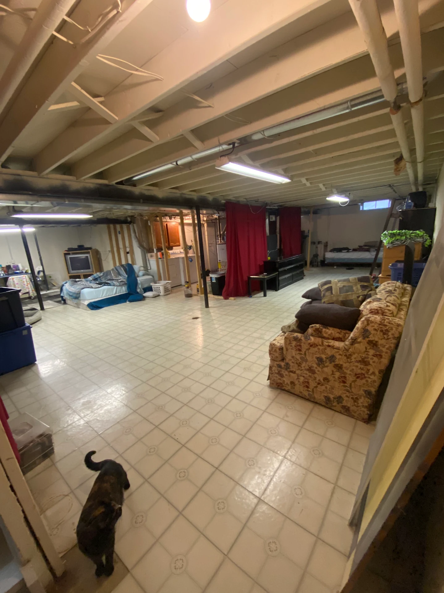 Unfinished basement with white tile floor, exposed pipes, and stored furniture